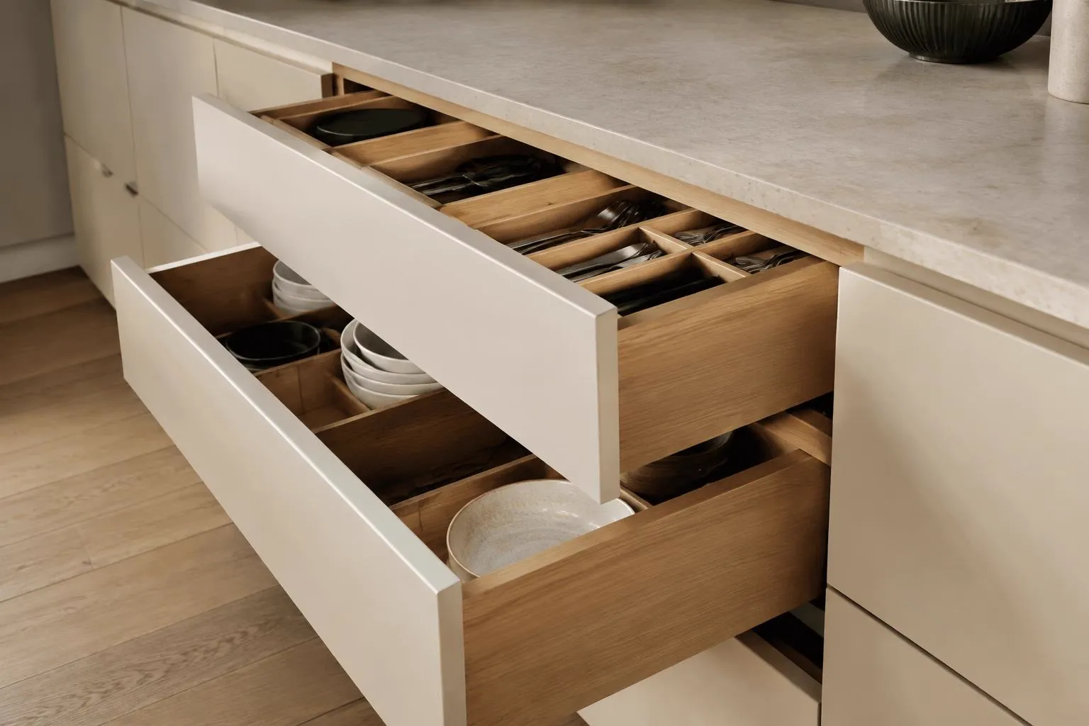 Open oak-lined drawers beneath an ivory kitchen counter with limestone top
